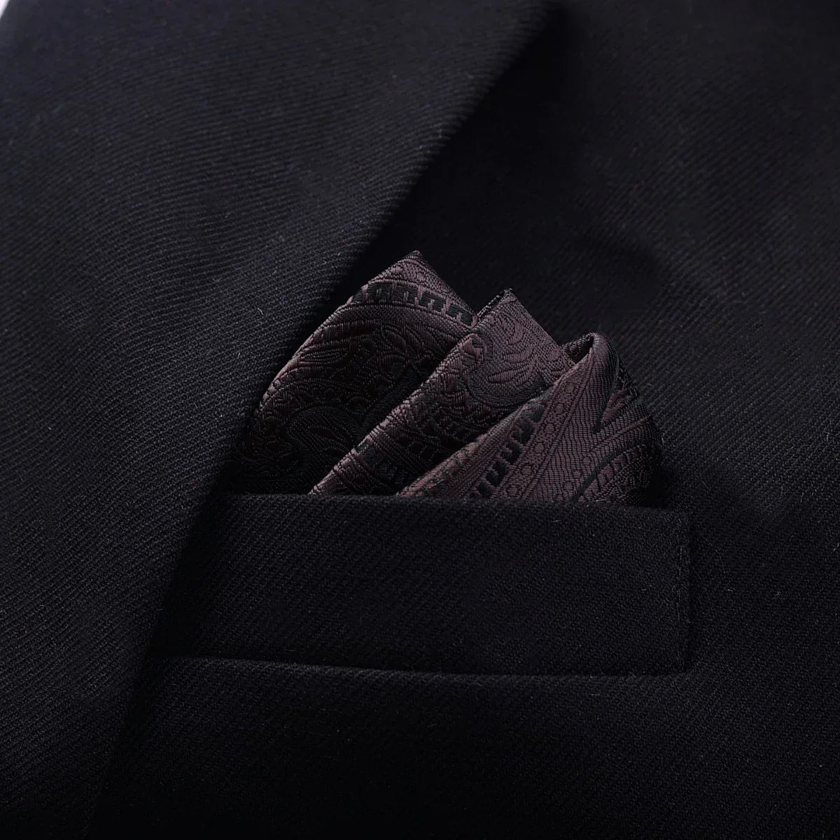 Black textured suit jacket with a dark paisley silk pocket square, close-up view