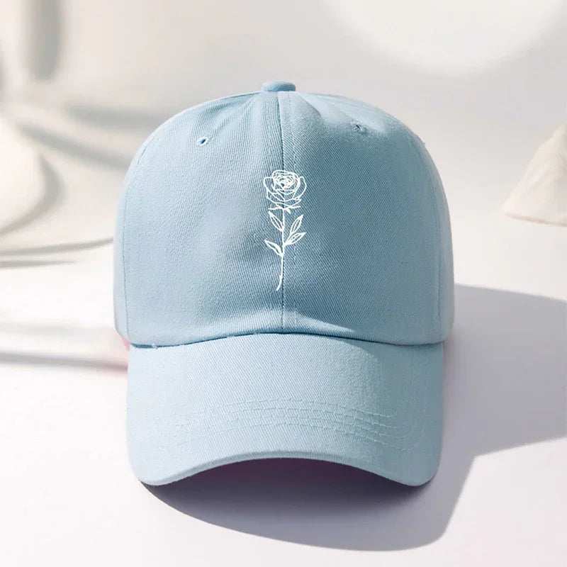 Light blue cotton baseball cap with white embroidered rose graphic, relaxed fit.