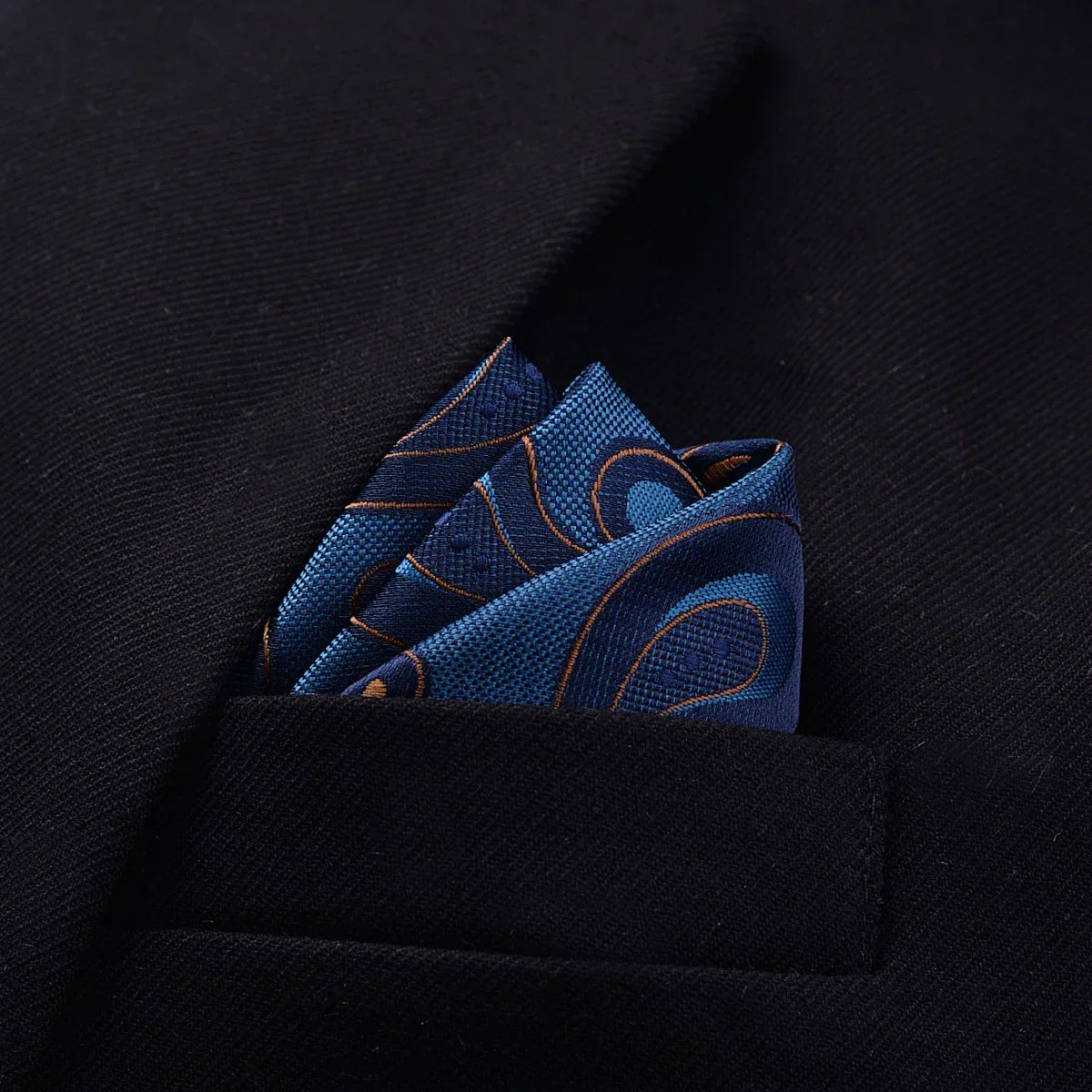 Navy blue patterned silk pocket square in black suit jacket pocket, folded neatly.