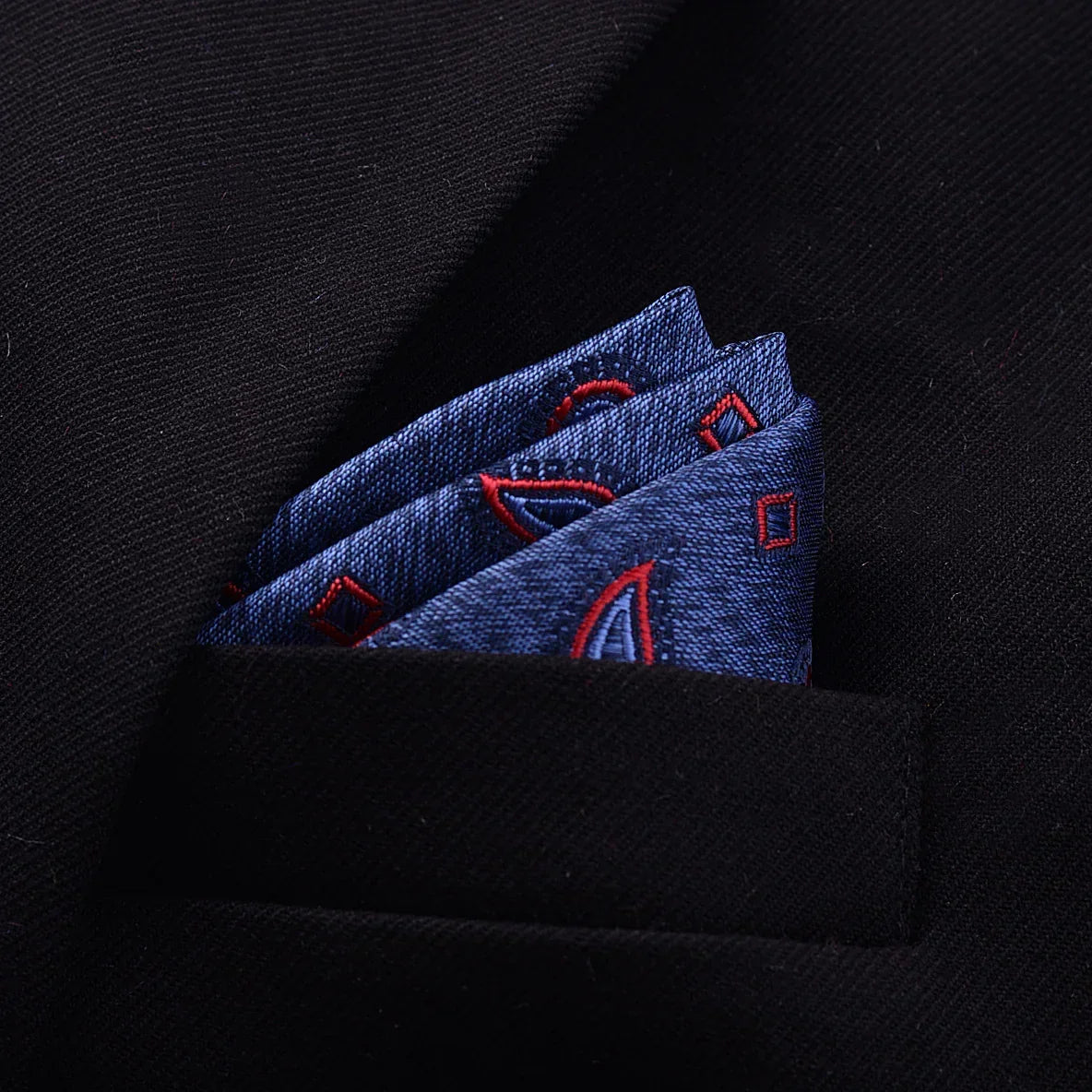 Blue denim pocket square with red embroidered geometric pattern in a black blazer pocket