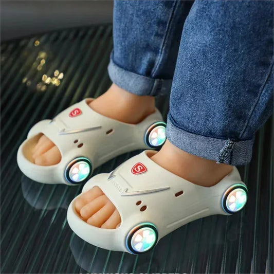 Child in rolled blue jeans wearing white slip-on sandals with colorful LED lights and car-shaped design