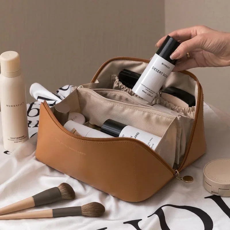 Tan leather cosmetic bag with beige interior, holding skincare bottles and makeup brushes on a cloth surface.