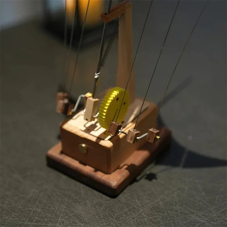 Handcrafted wooden kinetic sculpture with metal wires and yellow gear mechanism on a dark surface.
