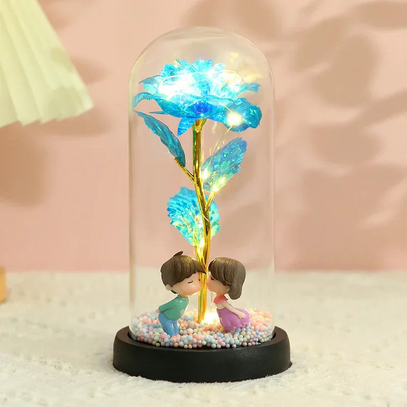 Illuminated glass dome with blue artificial flower and figurines, soft pink background.