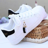 White low-top sneakers with black heel detail, lace-up style, and tassel accents