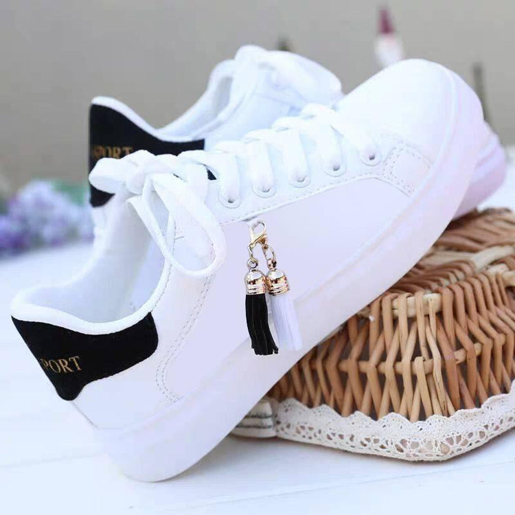 White low-top sneakers with black heel detail, lace-up style, and tassel accents