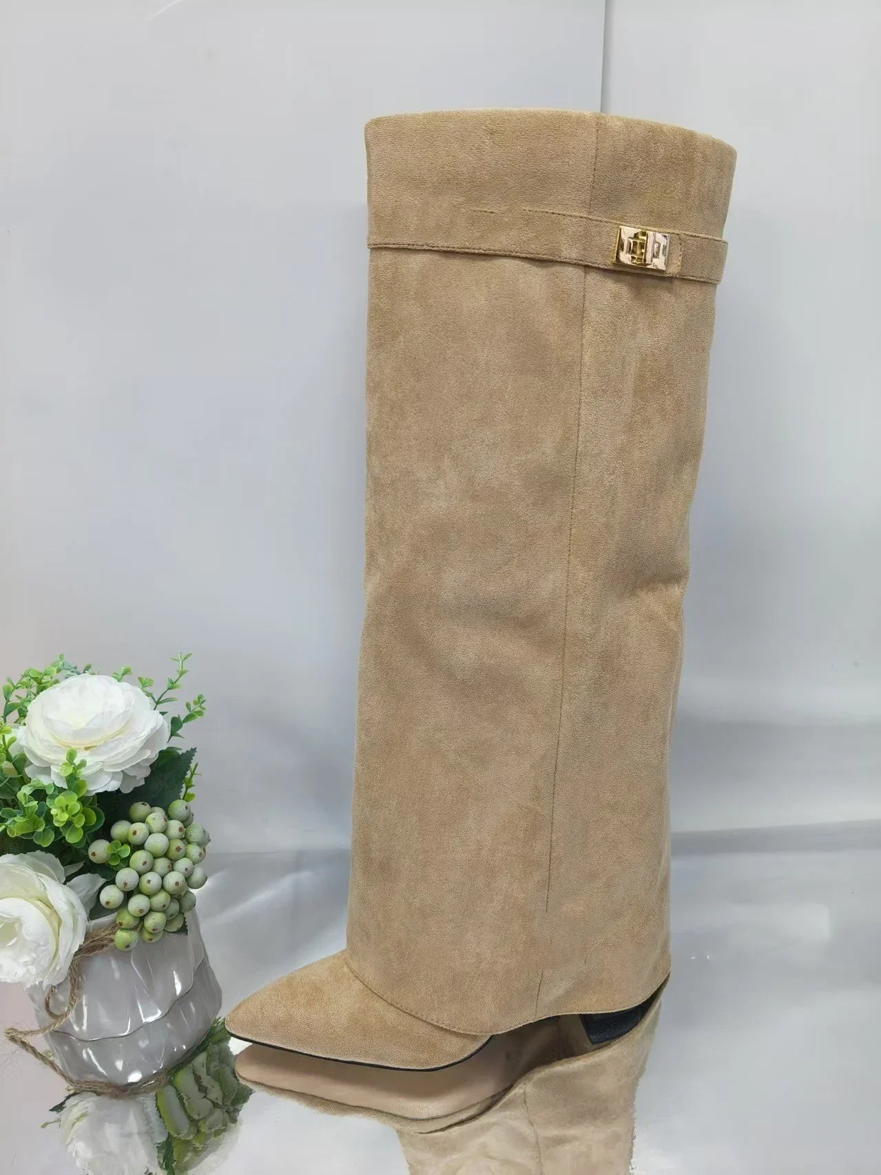Beige suede knee-high boot with pointed toe, slouchy fit, and gold buckle detail