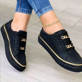 Black low-top sneakers with gold chain accents, gold trim, and lace-up design, worn with skinny jeans.
