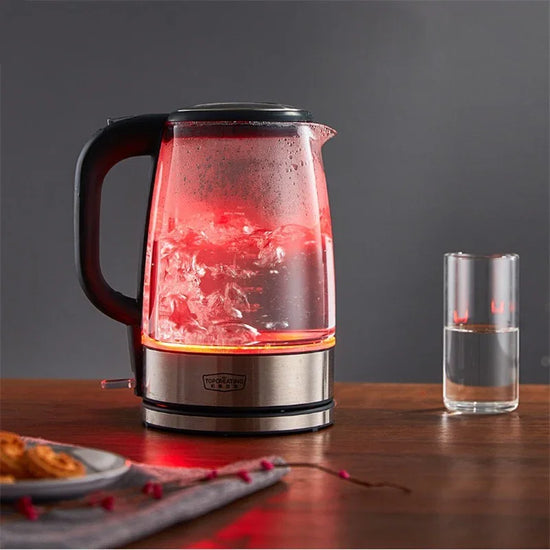 Glass electric kettle with boiling water and red LED light on wooden table