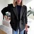 Woman wearing black double-breasted wool blazer with ribbed knit sleeves and relaxed fit.