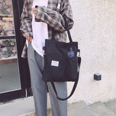 Casual streetwear outfit with loose plaid shirt, white tee, gray trousers, and black canvas tote bag