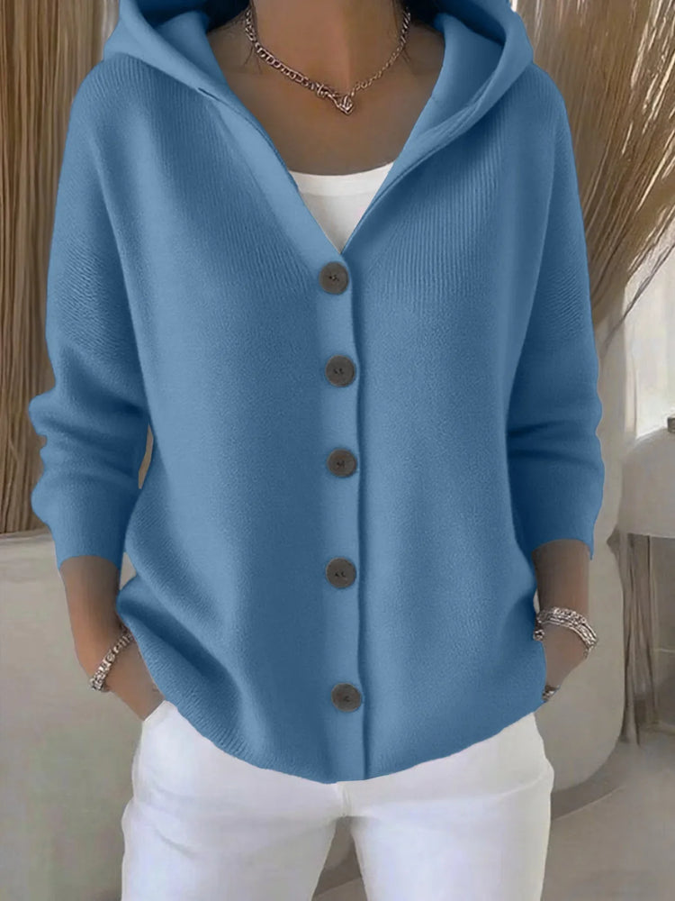 Woman wearing a relaxed-fit blue button-up knit hoodie with long sleeves and white pants.