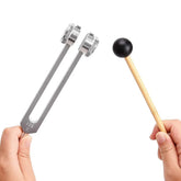 Hand holding metal tuning fork and wooden mallet with black rubber tip on white background