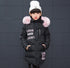 Girl wearing long black puffer jacket with pink faux fur hood, white beanie, and letter print.