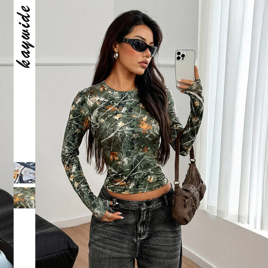 Woman wearing fitted long sleeve green camouflage print top with high-waisted dark jeans
