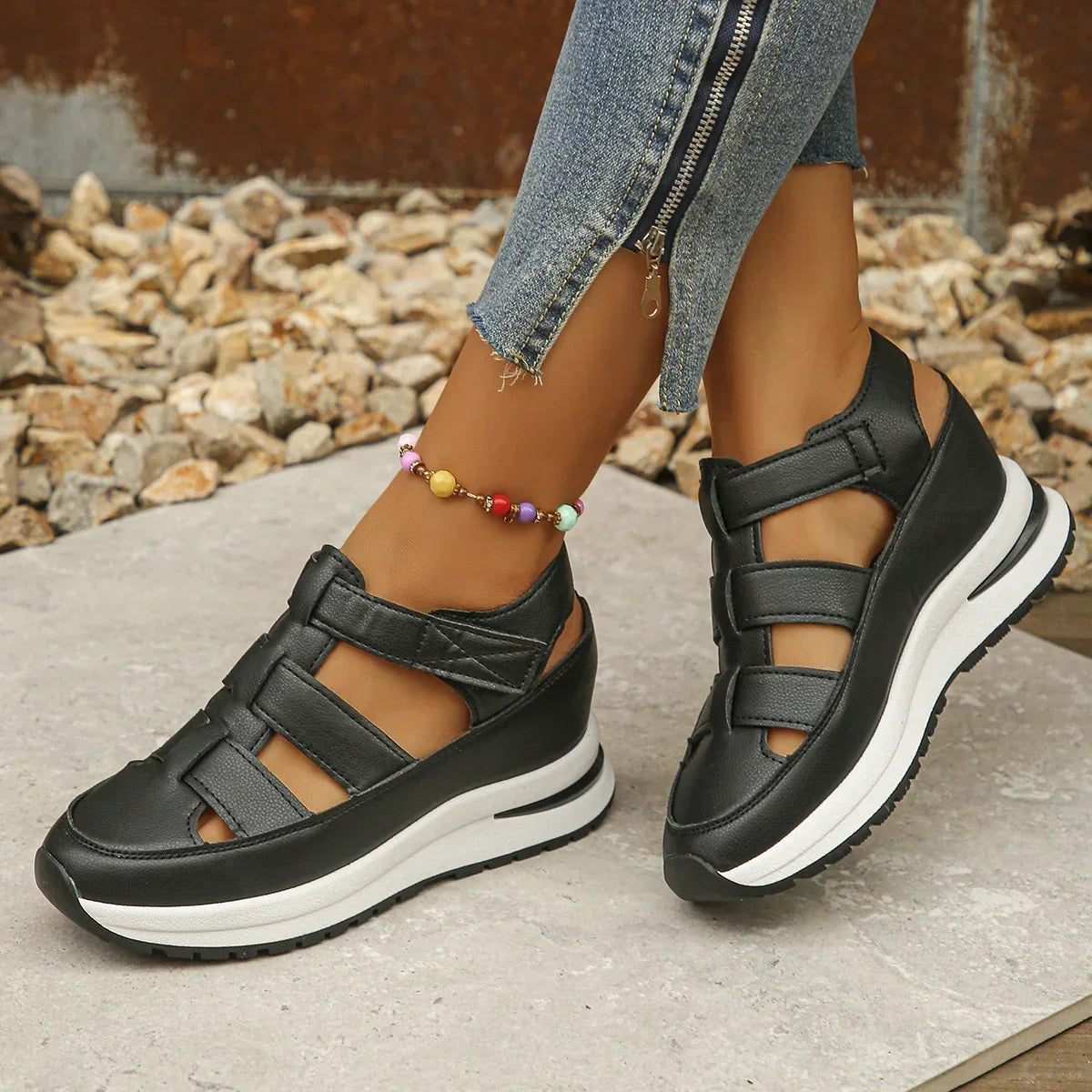 Black platform sandals with cut-out design and thick white sole, worn with zippered skinny jeans