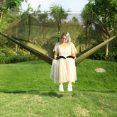 Woman in a sheer beige tulle dress and white sneakers reading on a green hammock outdoors