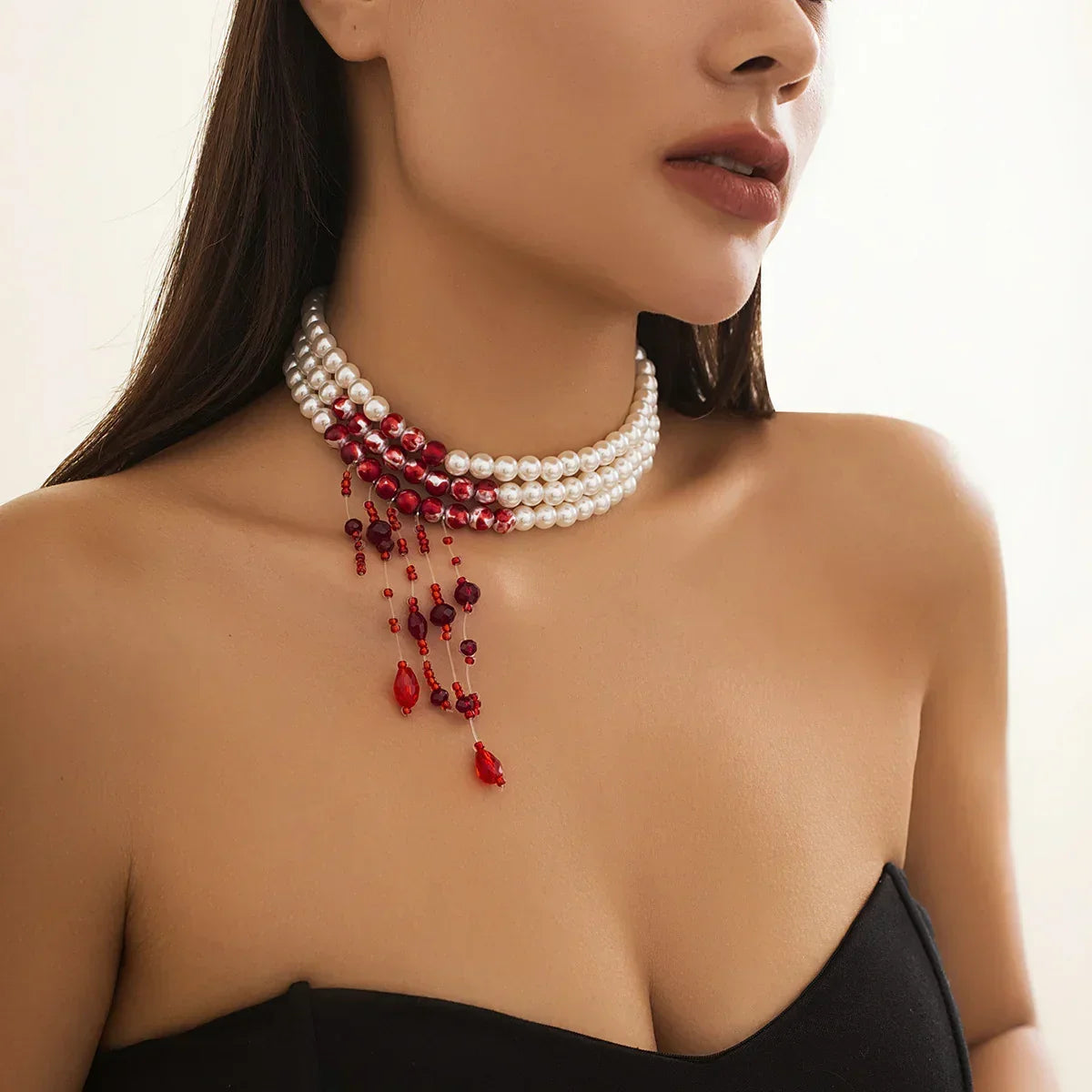 Woman wearing a strapless black top and layered pearl choker with red crystal accents