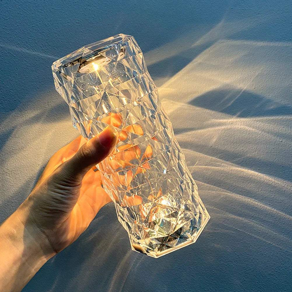 Hand holding a clear geometric LED table lamp with prism effect, casting light patterns on wall
