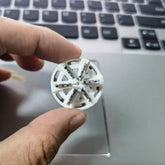 Hand holding a small white plastic wheel gear above a laptop keyboard