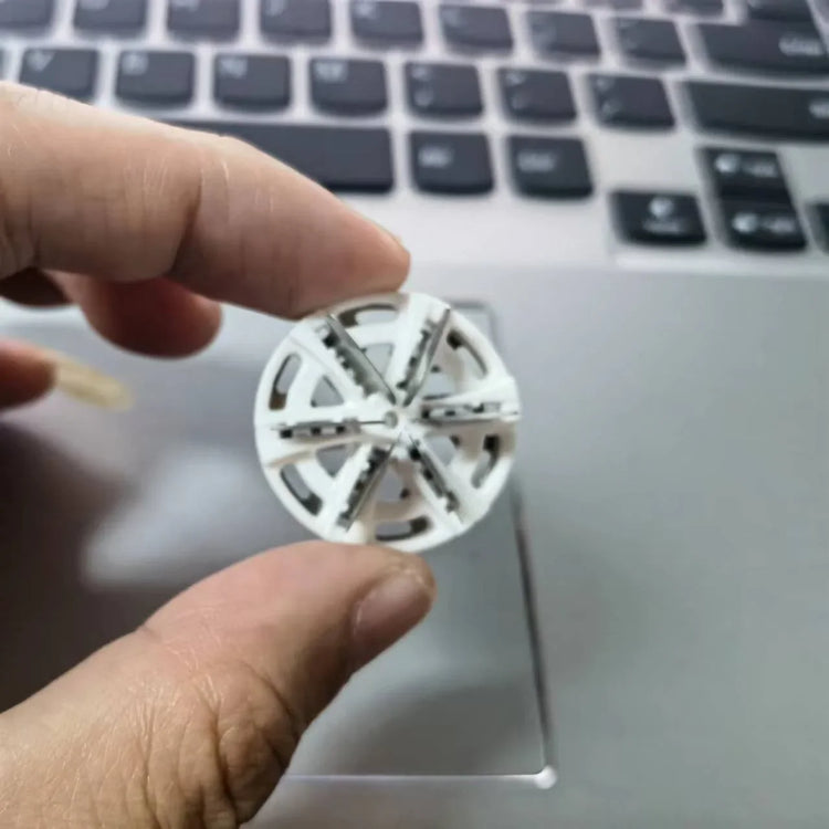Hand holding a small white plastic wheel gear above a laptop keyboard