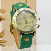 Vintage style watch with green leather strap, brass case, and musical notes dial.