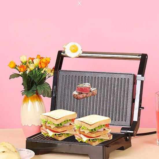 Double-decker grilled sandwiches with lettuce and deli meat on a black panini press, pink background.