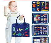 Toddler wearing light blue overalls and striped shirt, holding a navy blue dinosaur-printed educational felt activity book.