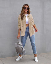 Woman in beige distressed shacket, white crop top, ripped blue jeans, and white sneakers
