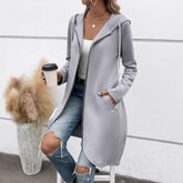 Woman wearing light gray hooded zip-up longline jacket, white tank top, and ripped blue jeans.
