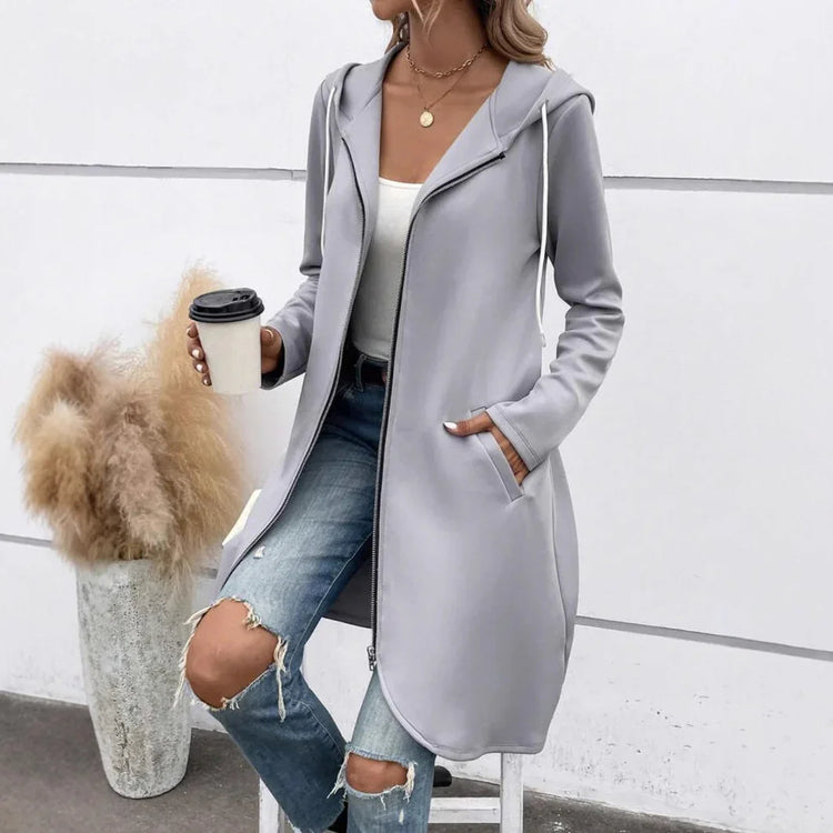 Woman wearing light gray hooded zip-up longline jacket, white tank top, and ripped blue jeans.