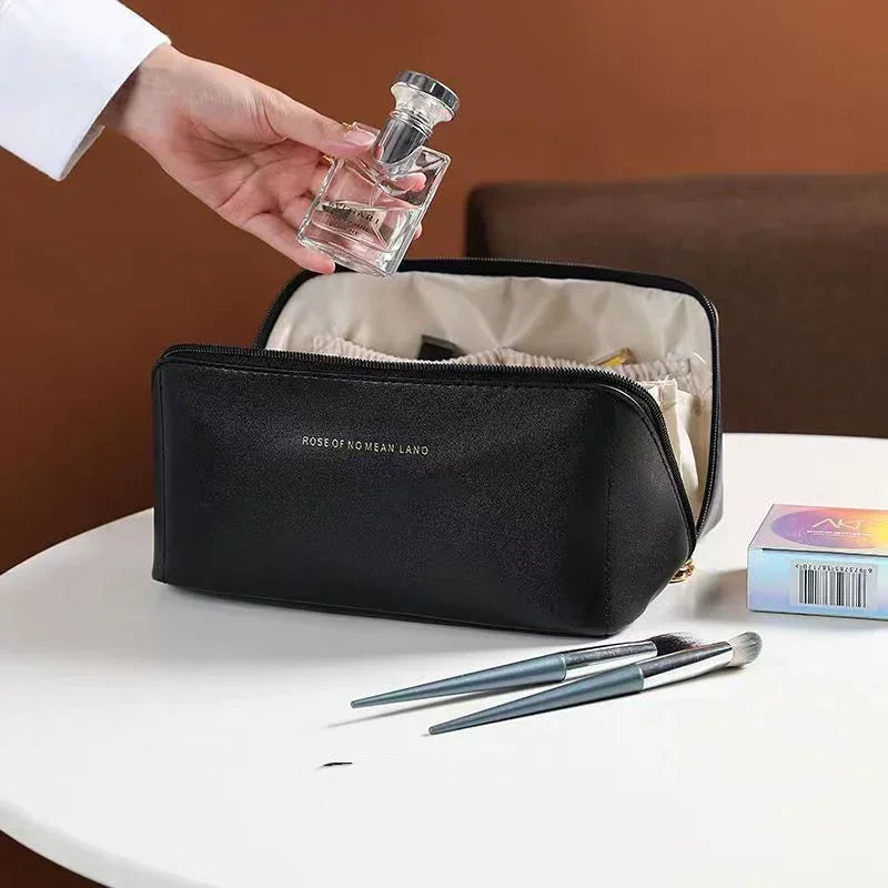 Black leather makeup bag with zipper, holding toiletries, on a table with brushes