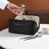 Black leather makeup bag with zipper, holding toiletries, on a table with brushes