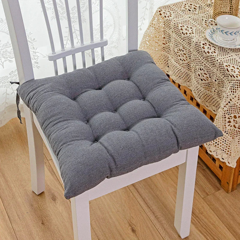 Plush grey tufted seat cushion on a white wooden chair, soft fabric, square shape, cozy fit.