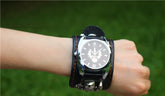 Black leather wide cuff wristwatch with bold face design, worn on wrist outdoors.