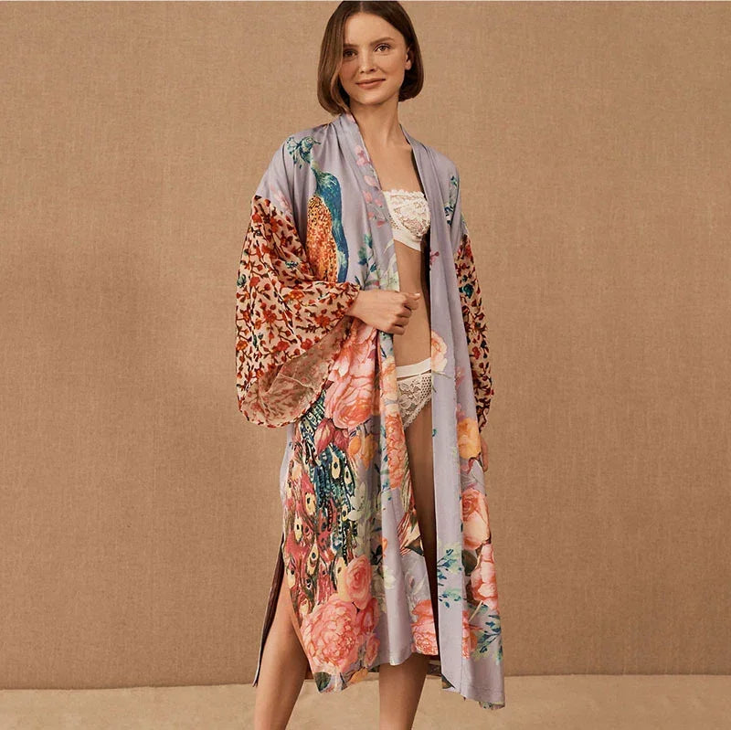 Woman wearing a long, loose satin robe with floral and peacock print in pastel tones