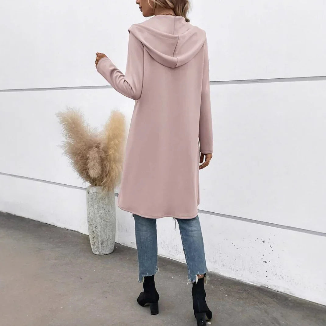 Woman wearing a long, light pink hooded sweatshirt, blue jeans, and black boots, relaxed fit