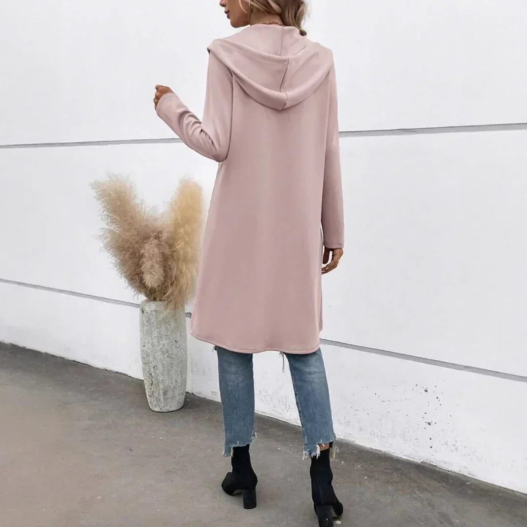 Woman wearing a long, light pink hooded sweatshirt, blue jeans, and black boots, relaxed fit