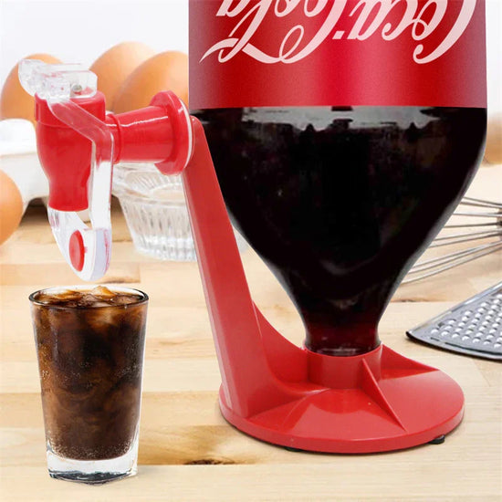 Red plastic soda dispenser holding an upside-down bottle, pouring cola into a glass on a kitchen table.