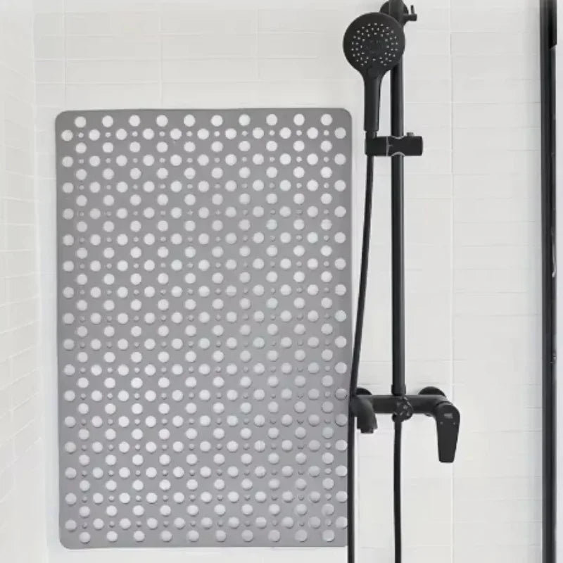 Gray non-slip rubber shower mat with circular holes on white tile, next to black shower head