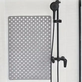 Gray non-slip rubber shower mat with circular holes on white tile, next to black shower head