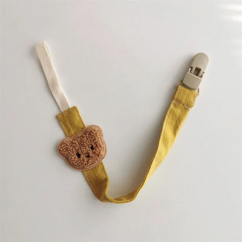 Yellow fabric pacifier clip with bear patch, soft material, metal clasp, modern baby accessory