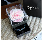 Light pink preserved rose in clear acrylic box with velvet jewelry drawer containing blue charm bracelets