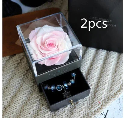 Light pink preserved rose in clear acrylic box with velvet jewelry drawer containing blue charm bracelets