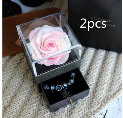 Light pink preserved rose in clear acrylic box with velvet jewelry drawer containing blue charm bracelets