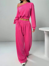 Woman wearing loose fit hot pink off-shoulder sweatshirt and wide-leg sweatpants set.