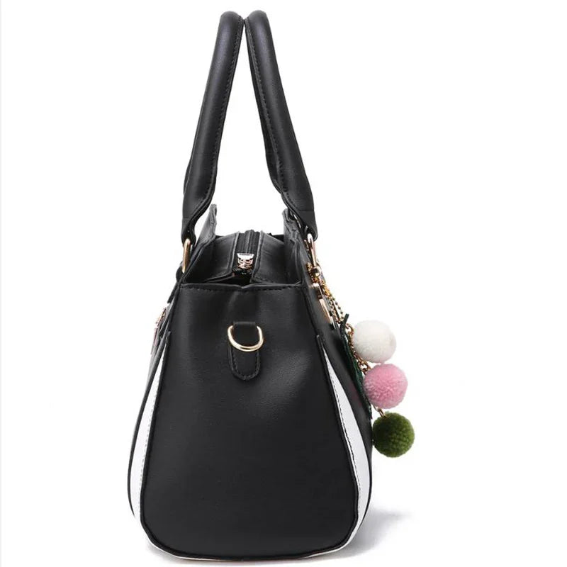 Black and white faux leather handbag with double handles and colorful pom pom charms