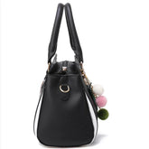 Black and white faux leather handbag with double handles and colorful pom pom charms