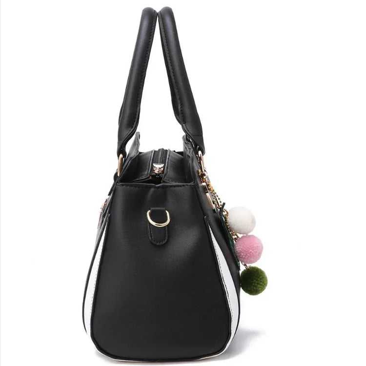 Black and white faux leather handbag with double handles and colorful pom pom charms