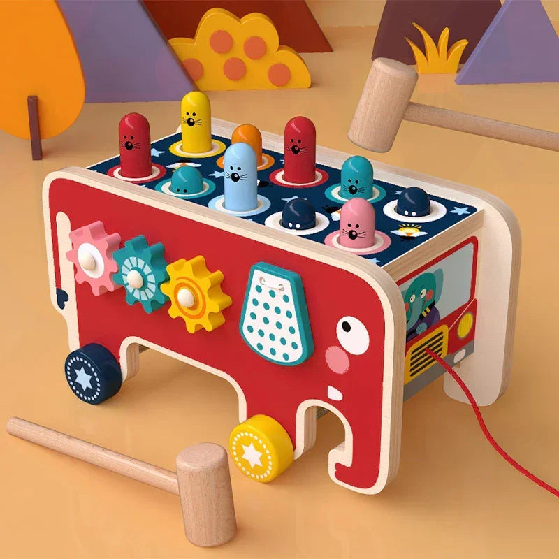 Colorful wooden toddler toy with gears, mallets, and pop-up animal pegs shaped like a bus